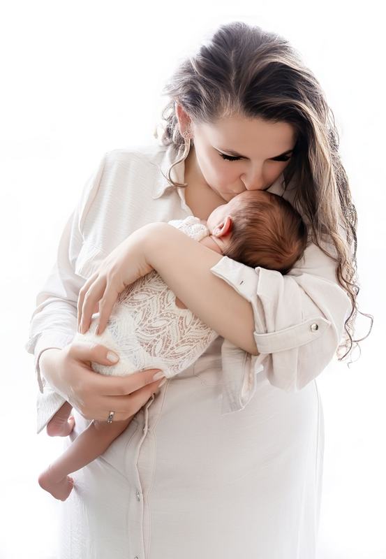 Vrouw in een witte jurk die een slapende baby wiegt en kust, tegen een helderwitte achtergrond.