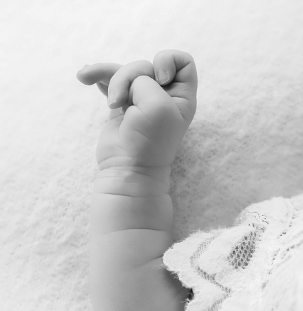 Het kleine handje van een baby reikt omhoog op een zachte deken, waar een kanten kledingstuk zichtbaar is.
