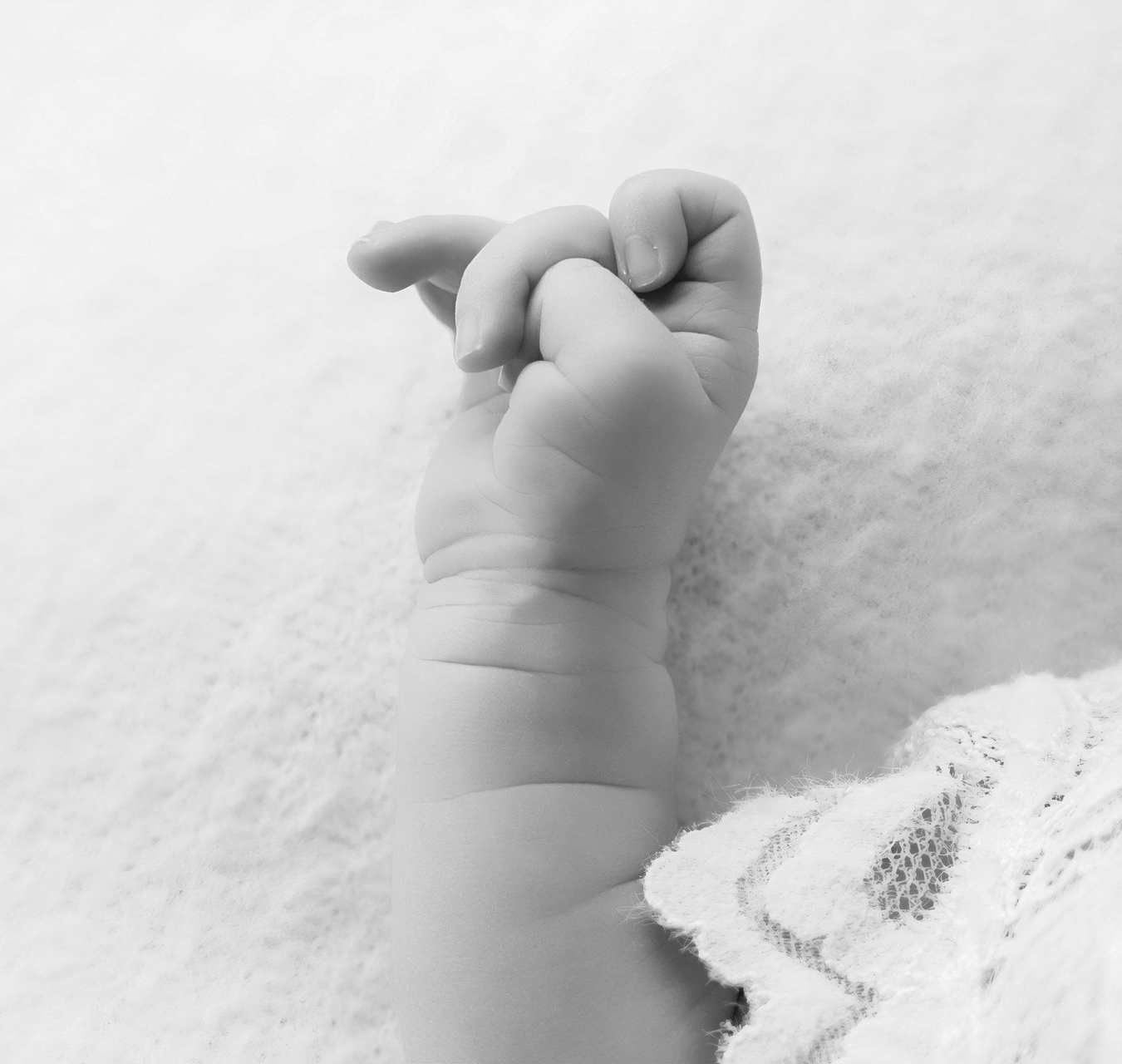 Klein babyhandje dat een volwassen vinger vastgrijpt op een zachte deken, in zwart-wit.