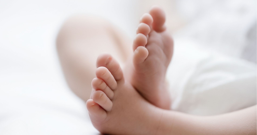 Twee blote voeten rusten op een wit bed, met een zacht vervaagde achtergrond.