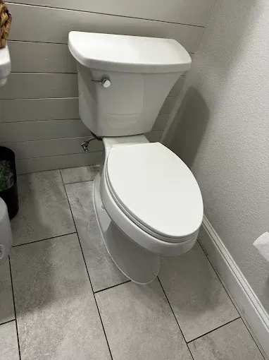 White toilet in a small tiled bathroom corner with a gray floor and wall.