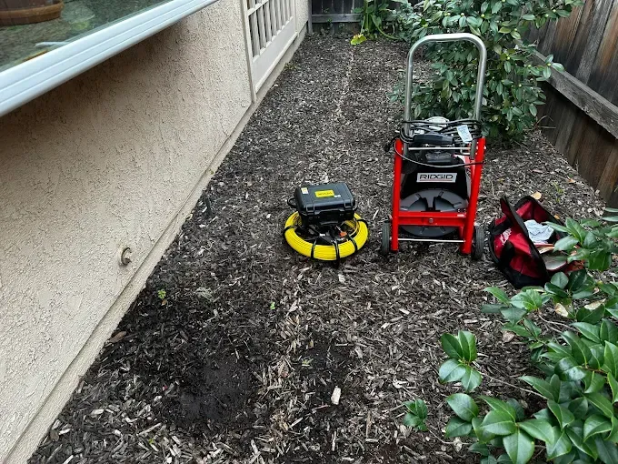 Lawn equipment on mulch beside a house: red cart, yellow blower, and red tool bag near bushes.