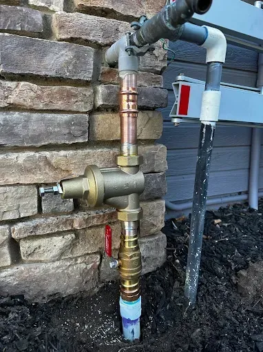 Outdoor water pipes and valves mounted beside a stone wall and house siding