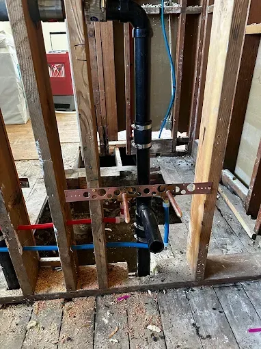 Exposed black PVC drain pipes and copper lines inside unfinished wall framing