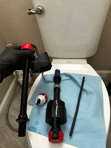 Toilet tank parts laid out on a bathroom floor with tools and a blue towel