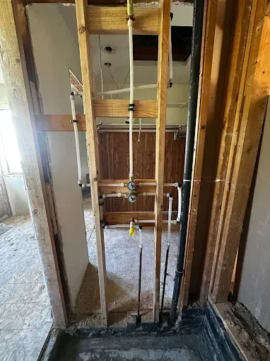 Framed doorway in a house under renovation, with exposed studs and plumbing in a narrow hallway