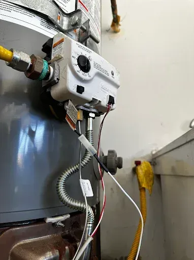 White utility control unit with wires and tubing mounted on a metal tank in an industrial room