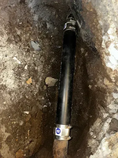 Black pipe with metal clamp in a dirt trench underground