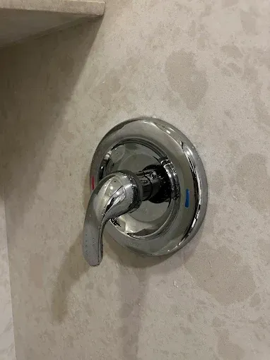 Chrome shower control handle on a beige tiled wall