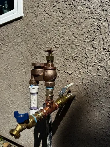 Metal outdoor water shutoff valve and pipes against a stucco wall, with blue and gold handles.