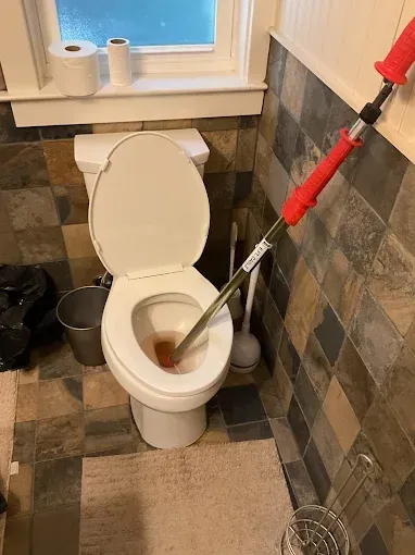 Bathroom toilet being plunged with a red-handled plunger; white toilet in a tiled room.