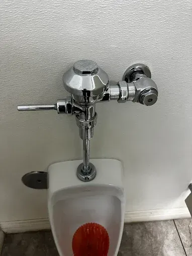 Wall-mounted urinal with chrome flush valve on a tiled restroom wall