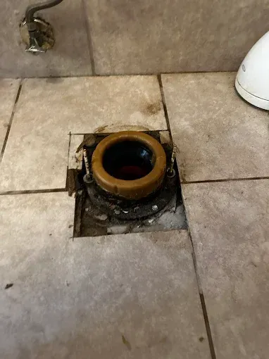 Open floor drain with a rust-colored ring in a tiled bathroom floor