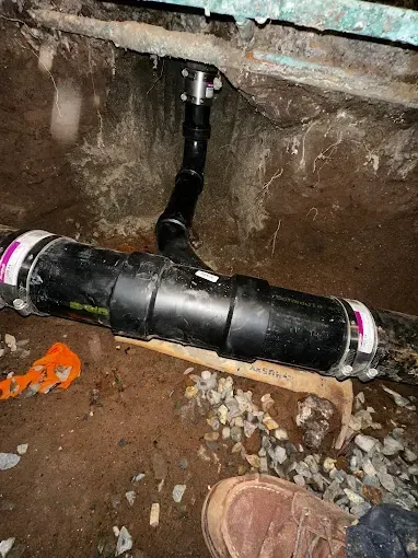 Black underground pipe connection in a dirt crawlspace under a house.