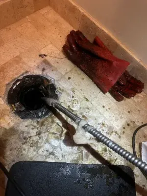 Clogged drain with a hose, red gloves, and a dark wet floor in a utility area