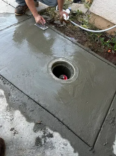 Person smoothing wet concrete around a circular drain opening outdoors