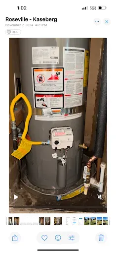 Water heater with labels and a yellow hose in a small utility closet.
