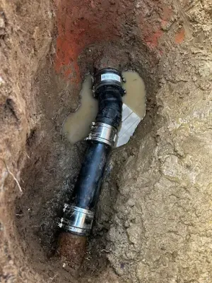 Black pipe repair in a muddy trench with metal couplings at both ends