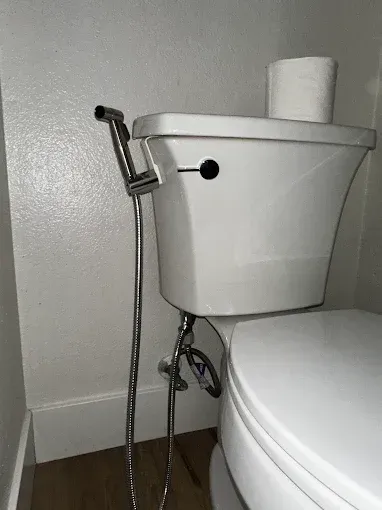 Toilet tank with bidet sprayer beside a toilet in a bathroom corner