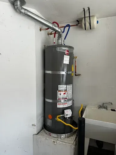 Water heater in utility room with silver venting, pipes, and a nearby sink