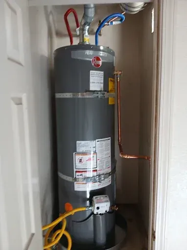 Water heater in a narrow utility closet with visible pipes and labels.