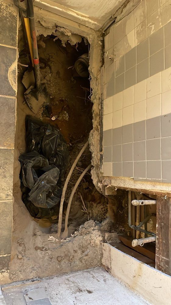 Partially demolished bathroom wall exposing pipes, rubble, and broken tile
