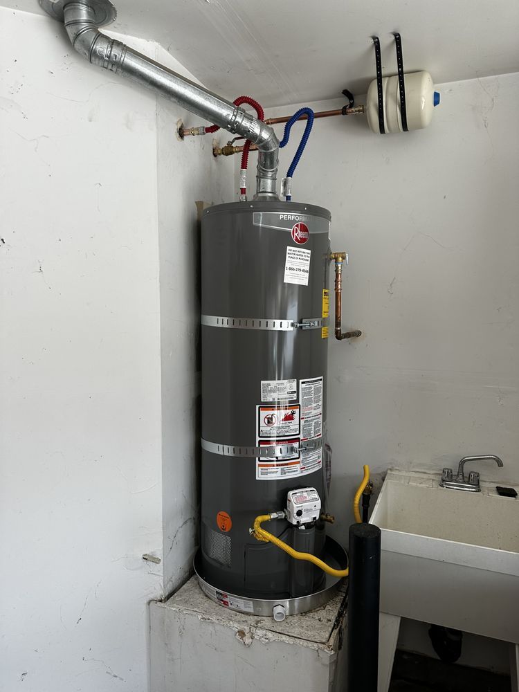 Water heater in utility closet with exposed pipes and ventilation ducting.
