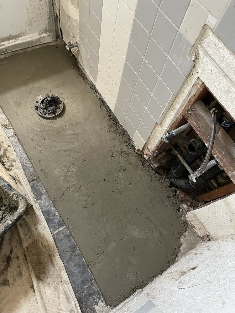 Freshly poured gray shower floor with a drain and exposed plumbing in a bathroom under renovation