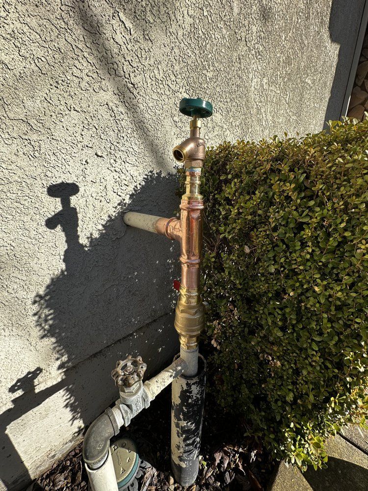 Outdoor copper water pipe with shutoff valve beside a wall and bushes