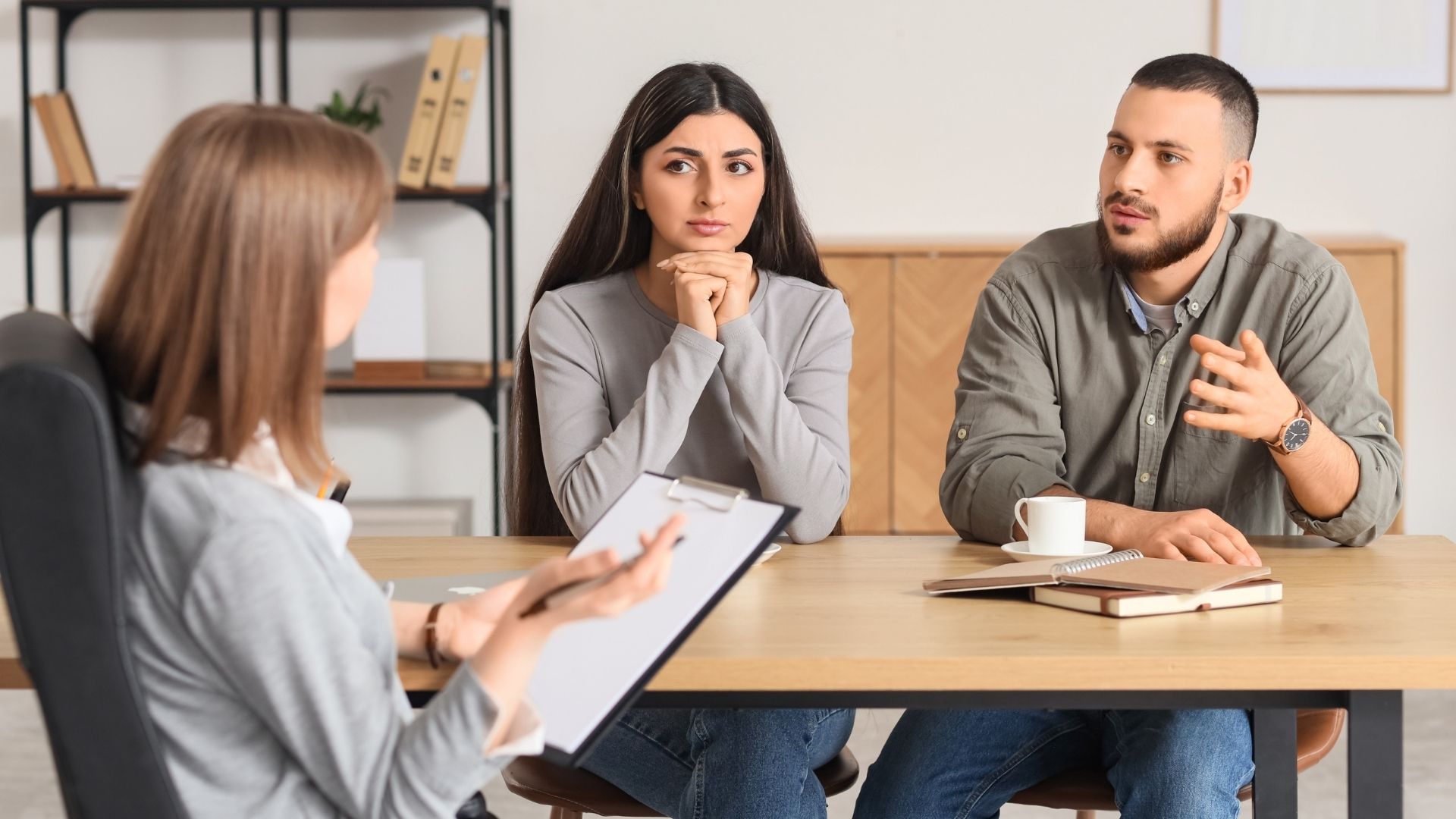 Counselor speaking with two clients at a table in a bright office, both listening attentively