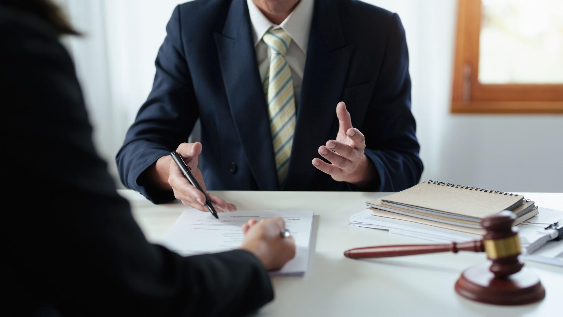 Business meeting with two people discussing documents, with a gavel on the table and a suit-clad speaker.