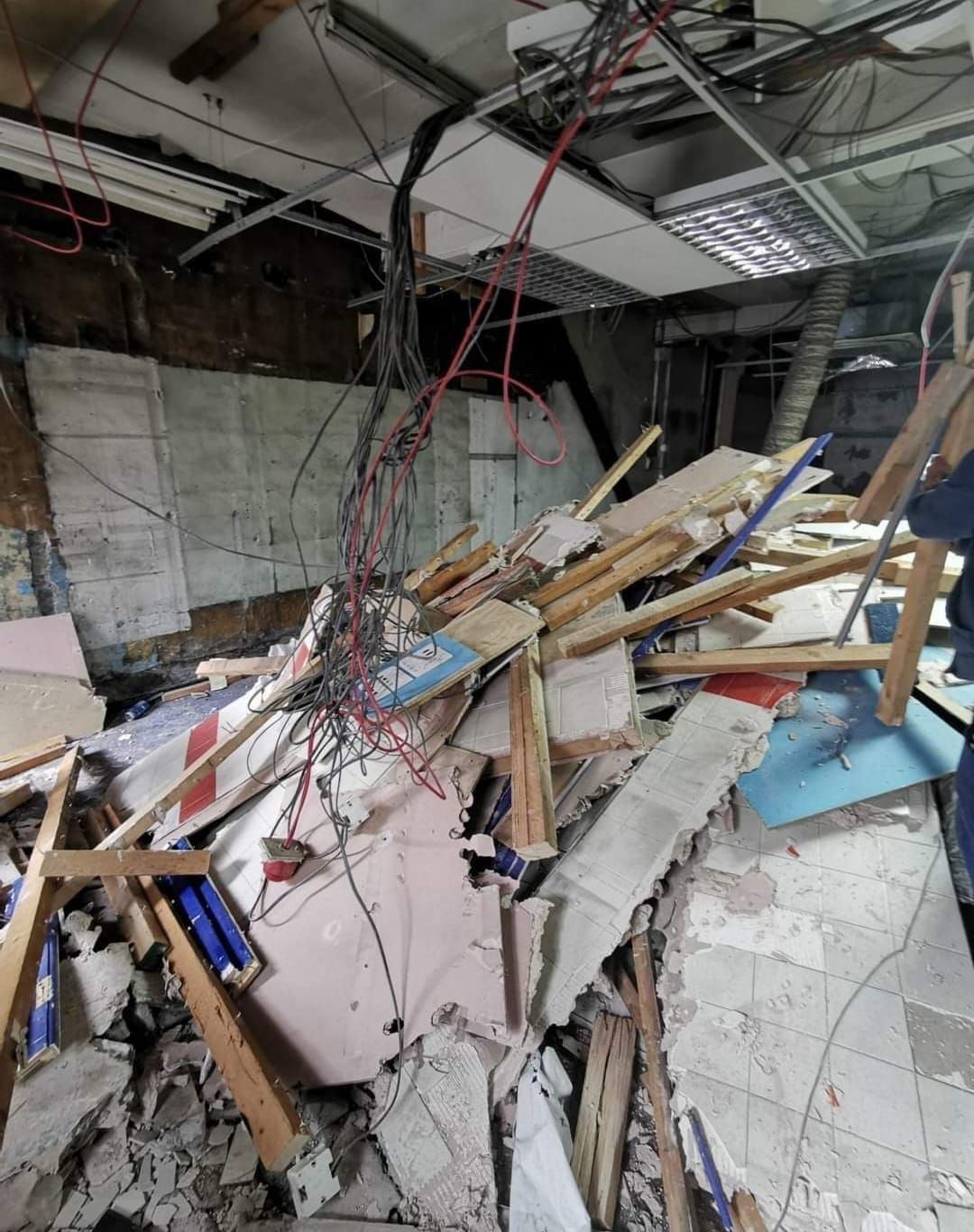 Interior view of a collapsed building. Debris, wires, and exposed infrastructure are scattered throughout the space.
