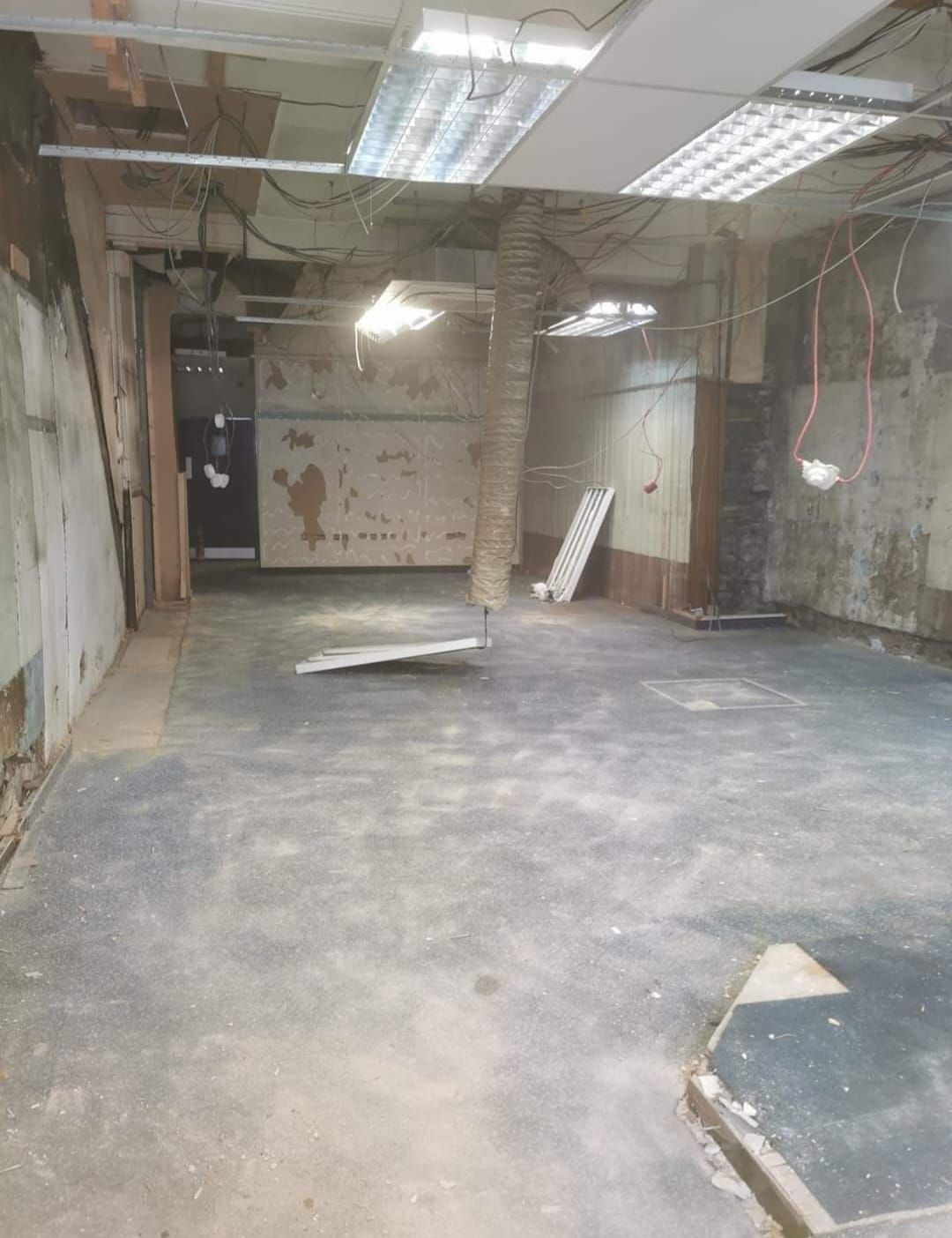 An empty interior space during renovation; exposed walls, ceiling fixtures, and concrete floor.