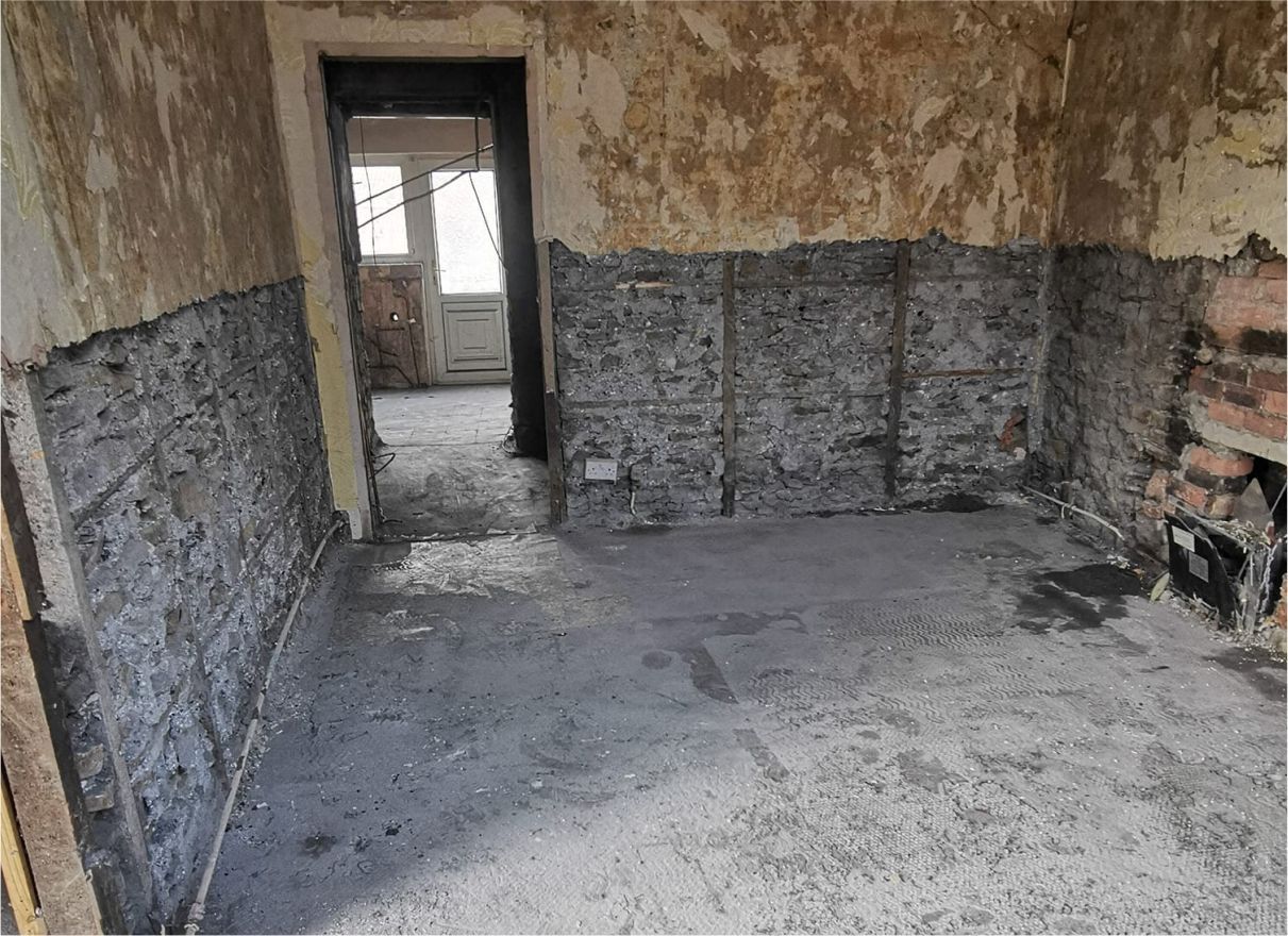 Interior of a room under renovation. Exposed brick walls are partially covered in gray plaster, with a doorway leading to another room.