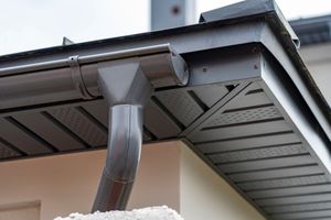 Gray gutter system on a house, with downspout and soffit.