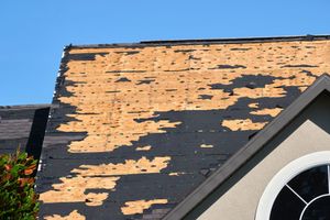 Damaged asphalt shingle roof with missing sections, revealing the wood substrate.