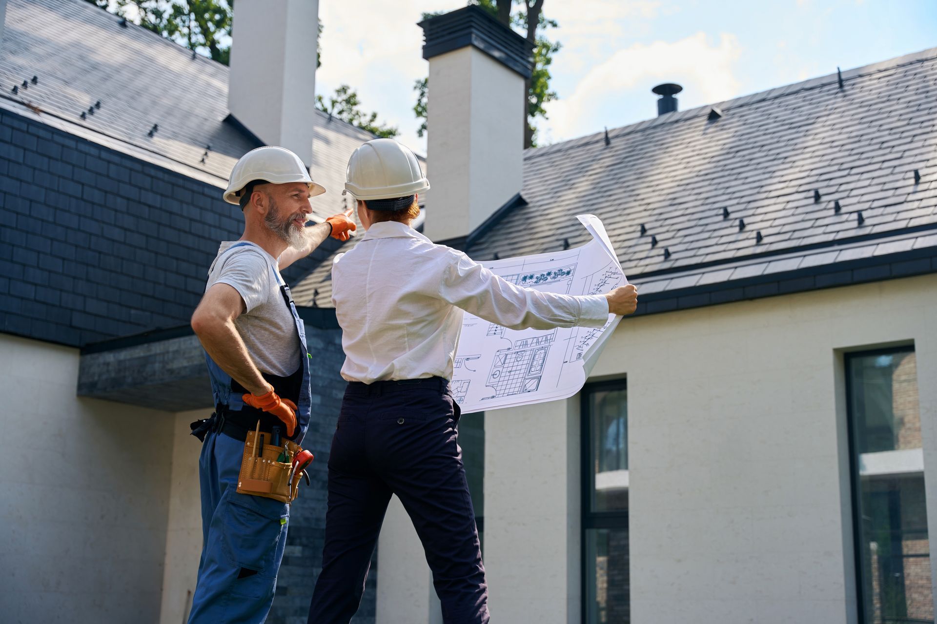 Two people in hard hats looking at blueprints on a rooftop near a chimney, discussing the construction of a building.