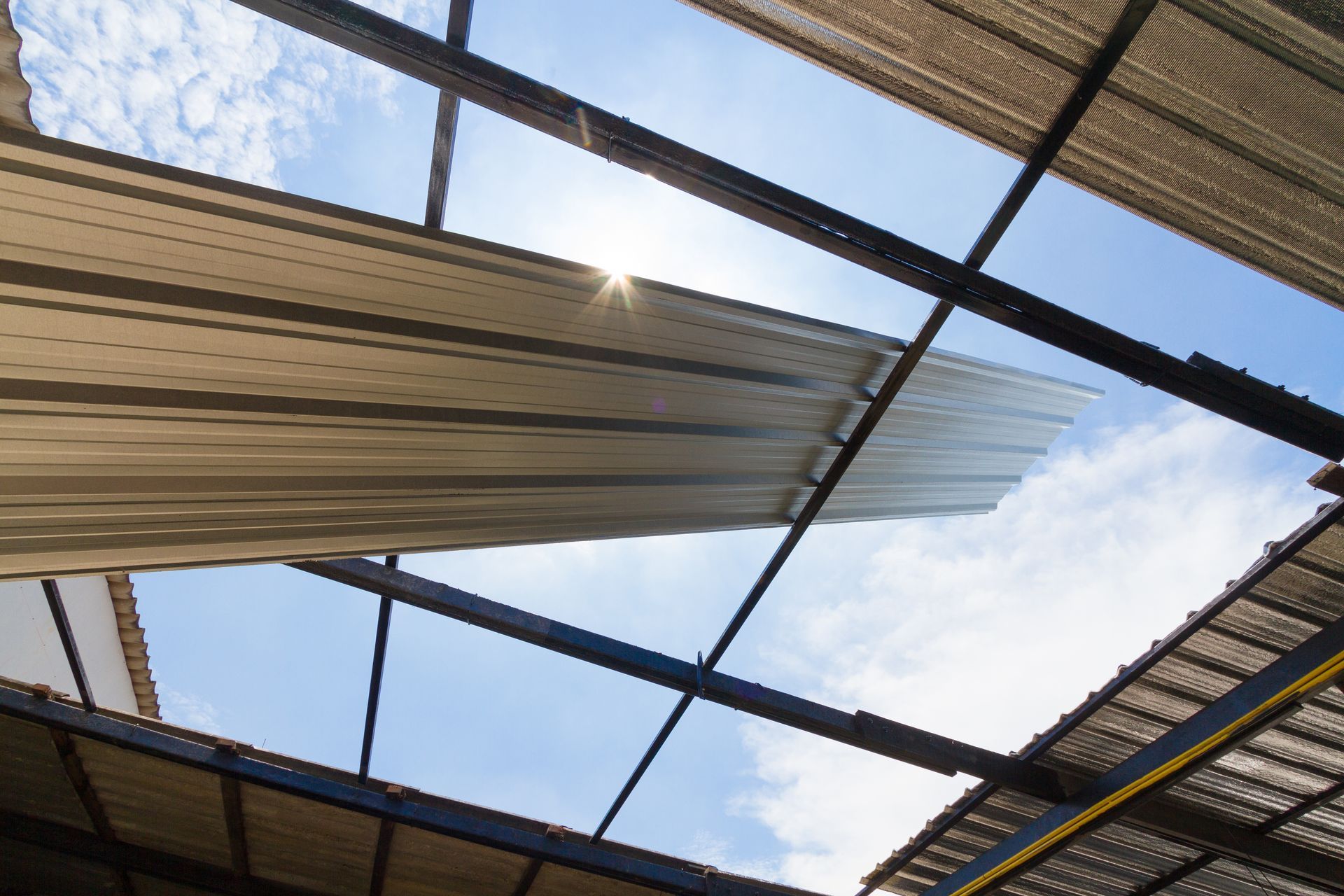 Sunlight through a damaged corrugated metal roof, angled view of a blue sky.