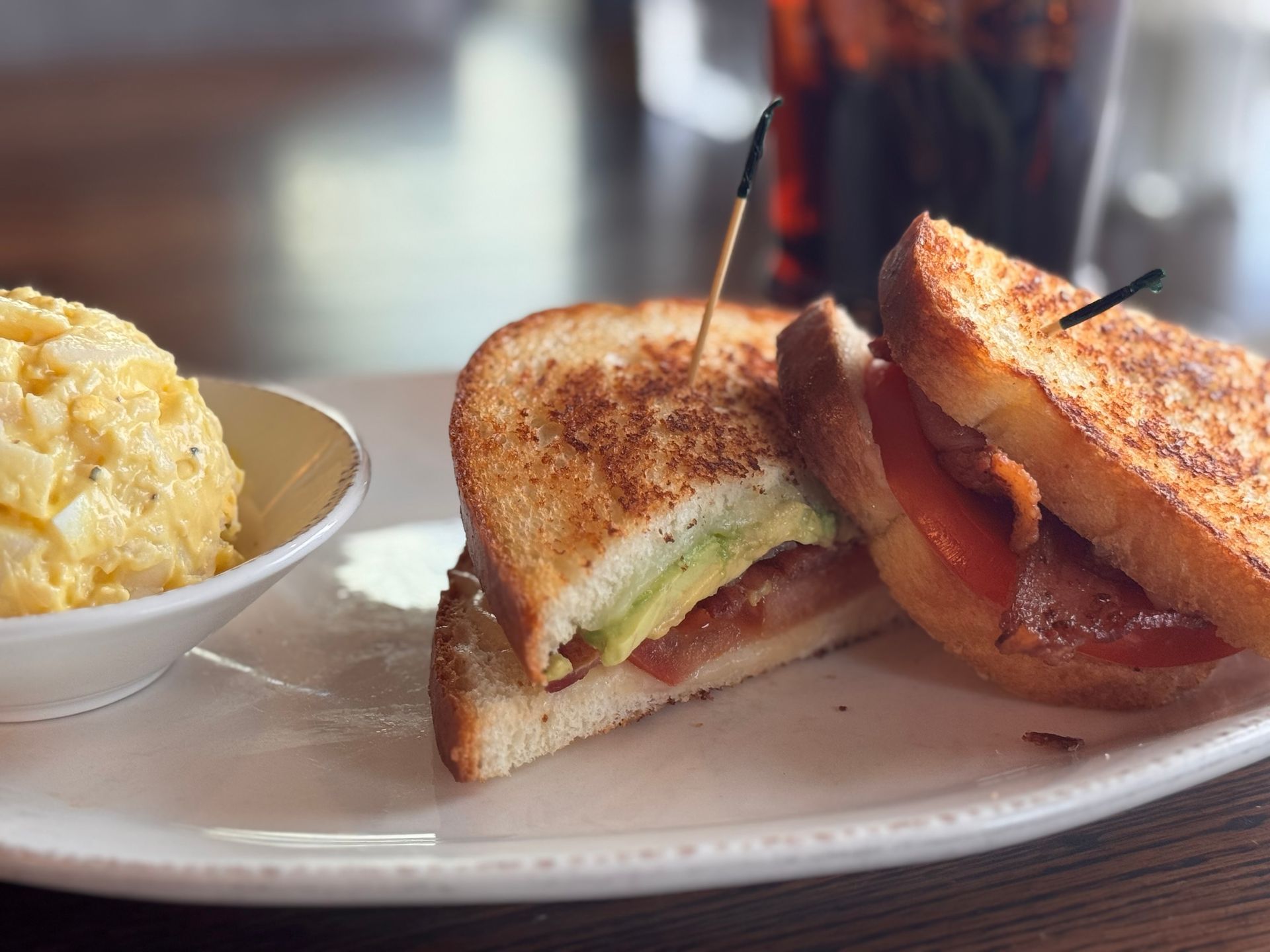 Grilled sandwich with avocado, tomato, and bacon, served with potato salad.