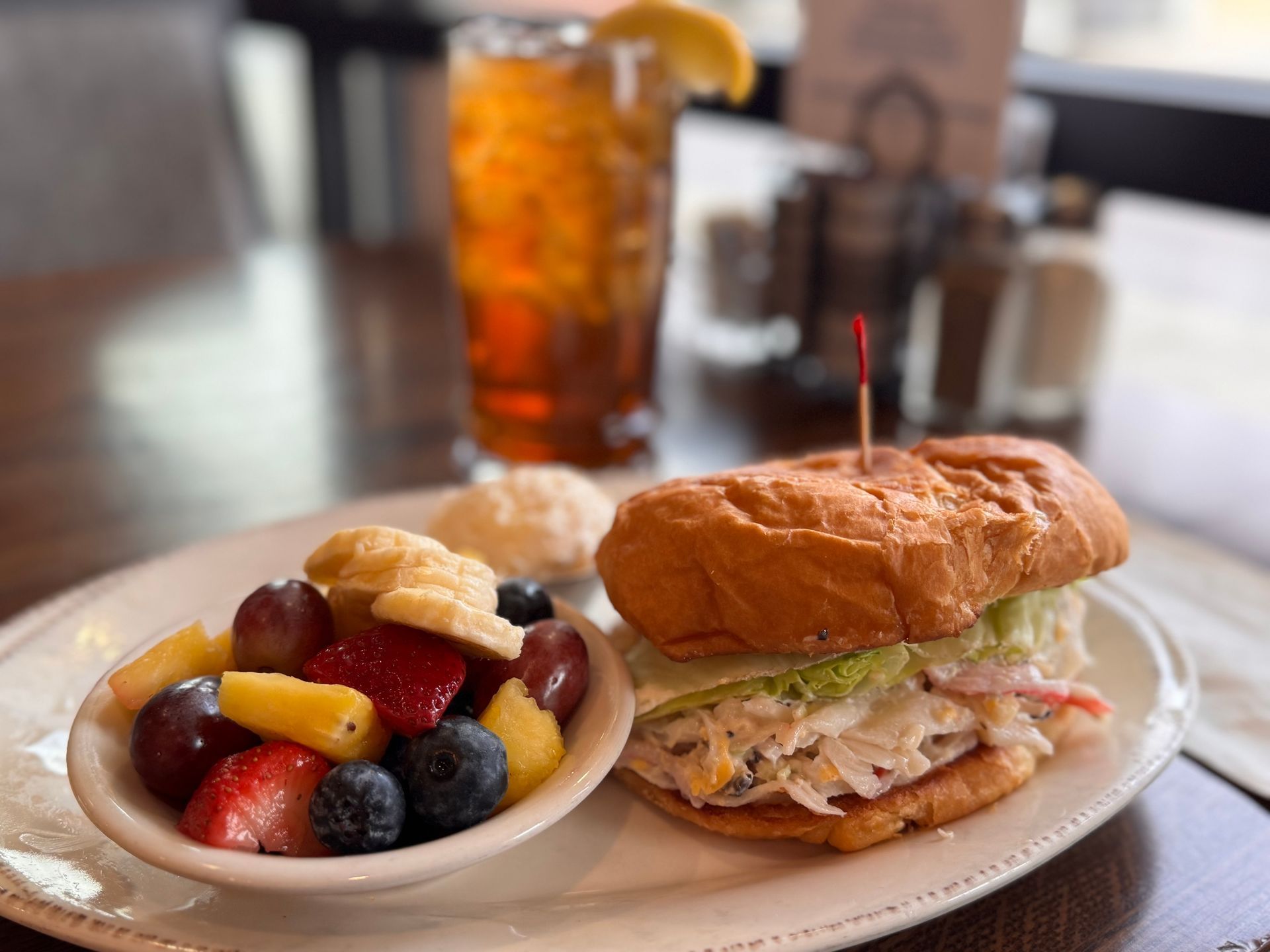 Sandwich, fruit salad, and iced tea on a plate in a restaurant setting.