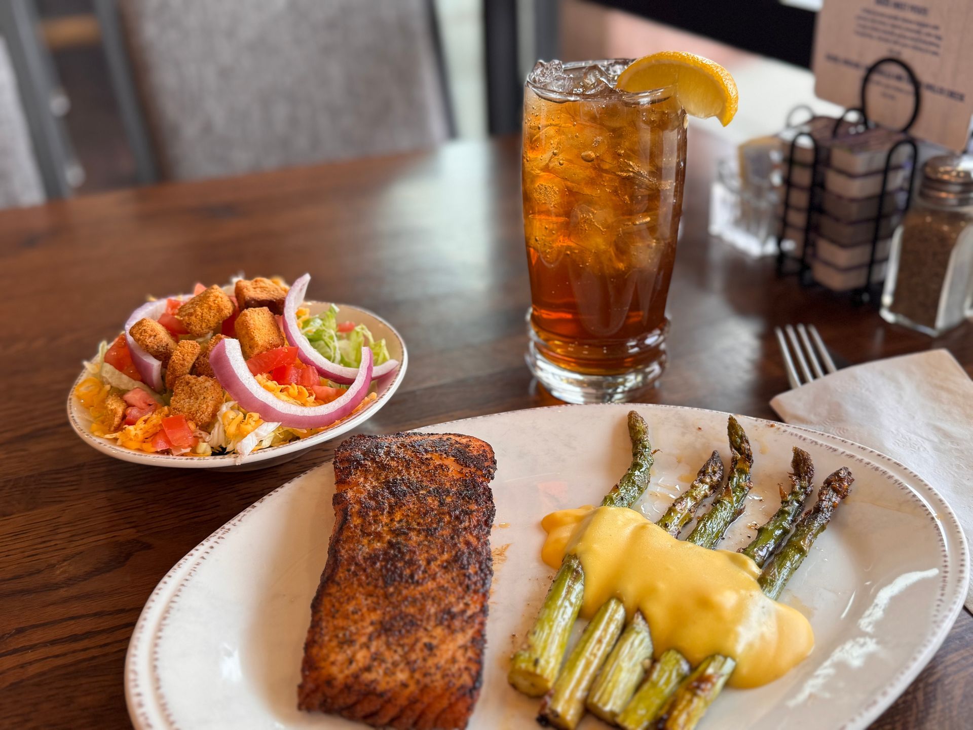 Salmon, asparagus with sauce, salad, and iced tea on a table.