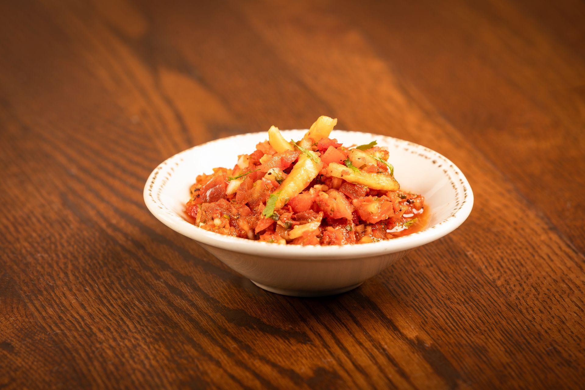 Bowl of chunky tomato and pepper salsa on a dark wooden table.