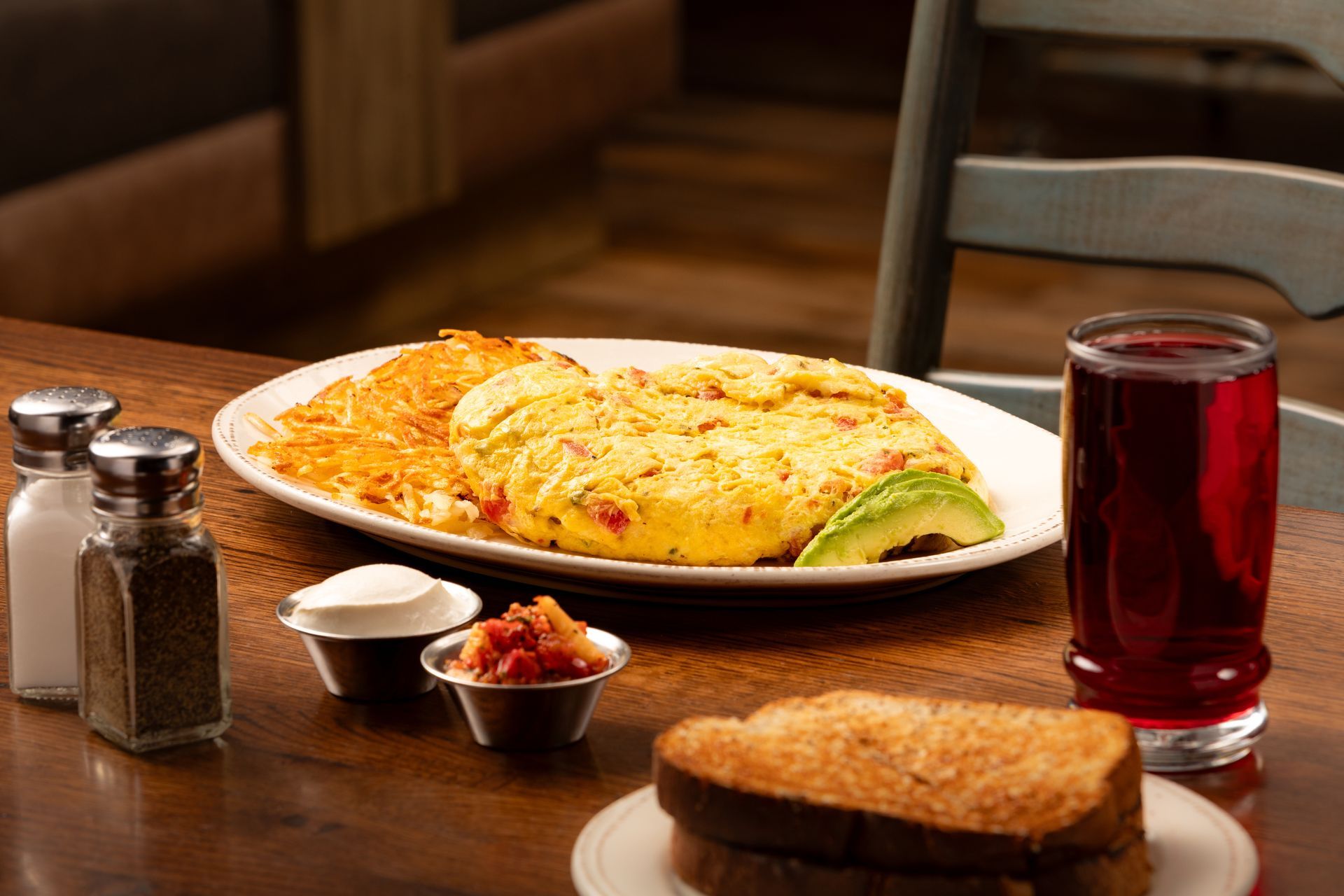 Restaurant table with omelet, toast, condiments, and a glass of red drink