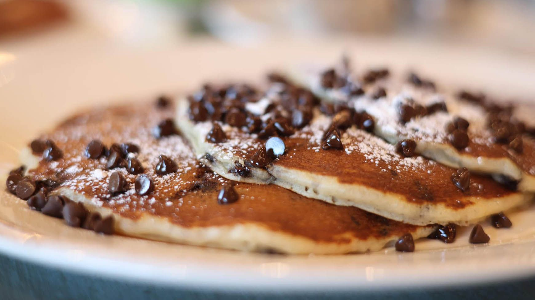 Stack of chocolate chip pancakes dusted with powdered sugar.