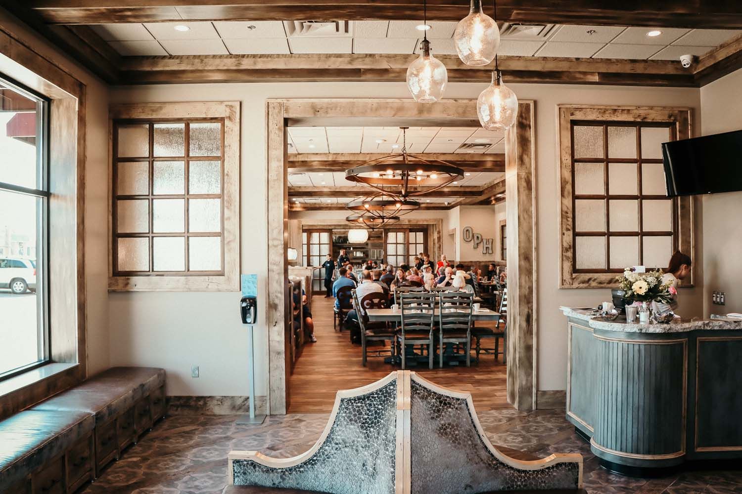 Restaurant interior with wooden beams, tables, and customers, and a decorative entrance.