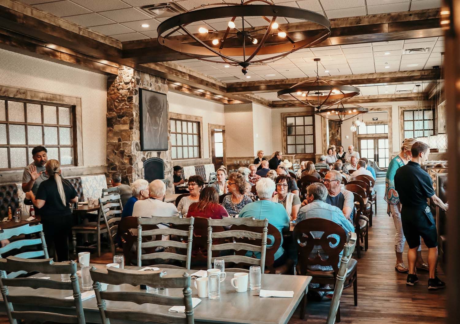 Restaurant interior with people seated at tables, wooden beams and chandeliers.