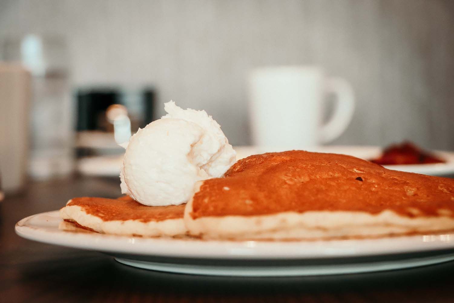 Pancakes topped with a scoop of white whipped cream on a white plate.
