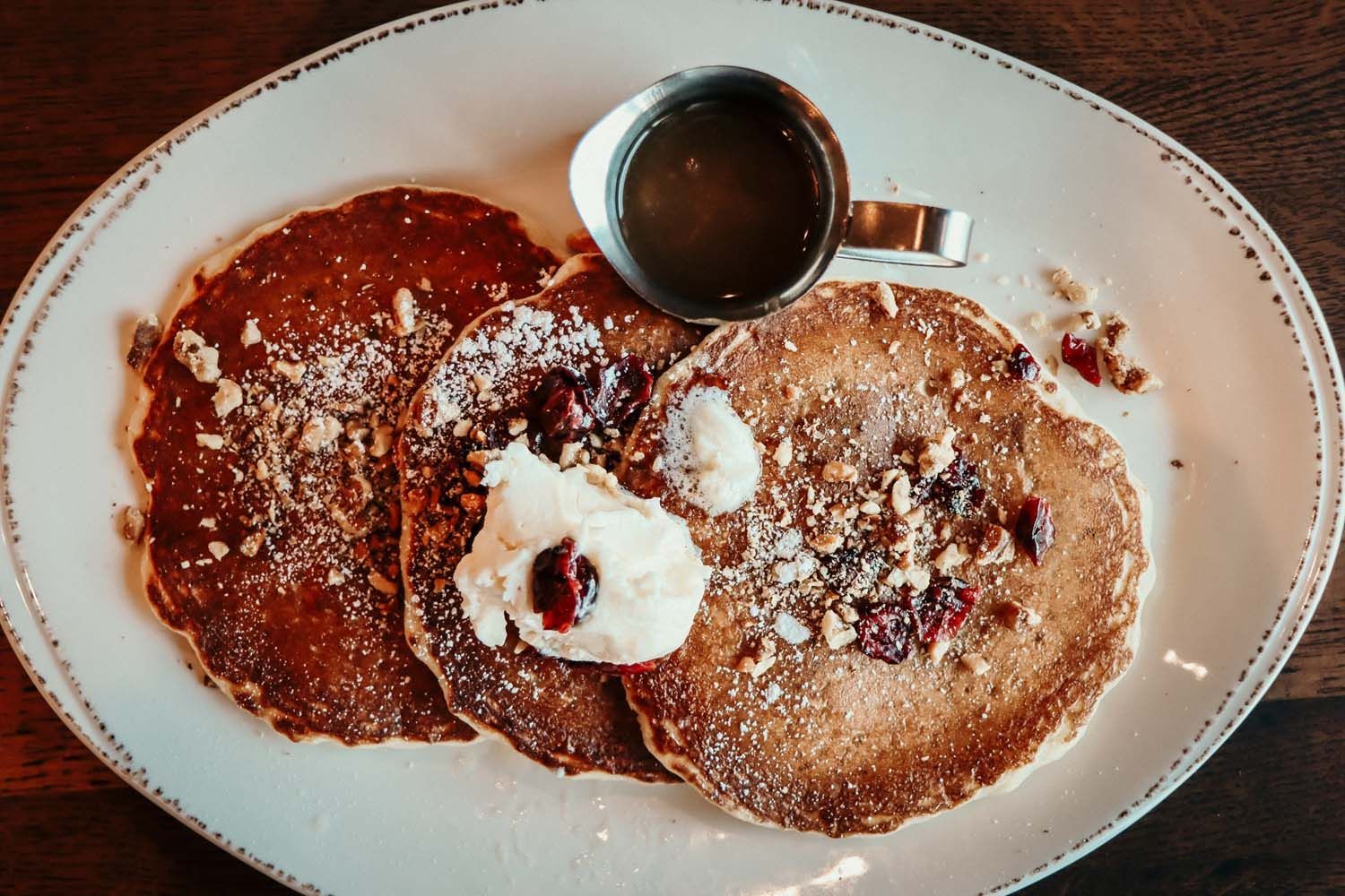 Three pancakes with toppings, syrup, and cream on a white plate.