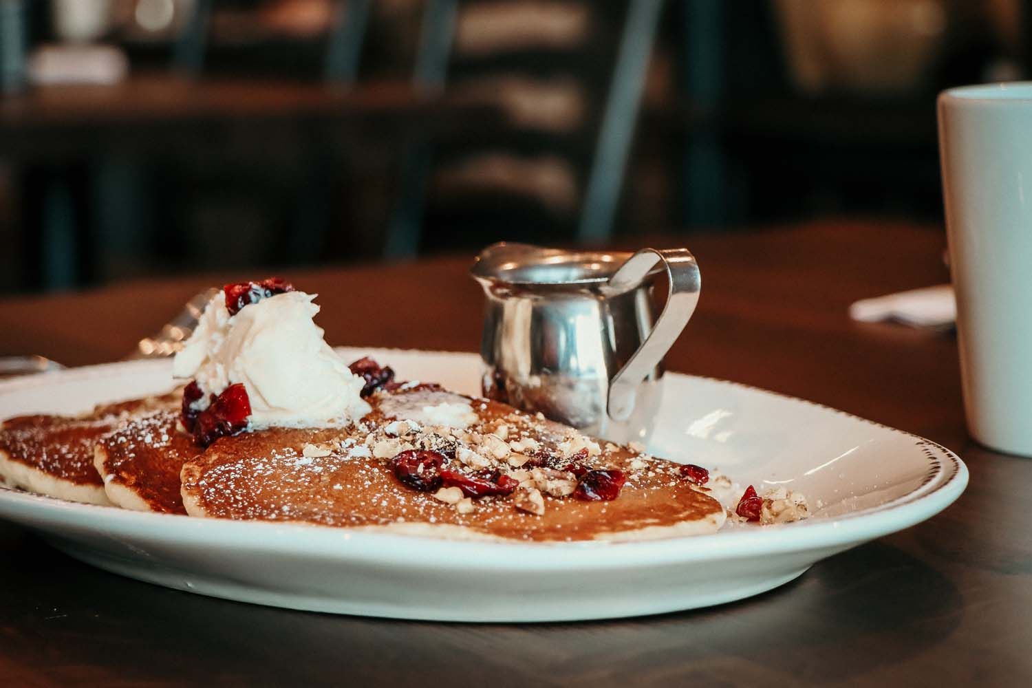 Pancakes with whipped cream, berries, and syrup on a white plate in a restaurant.