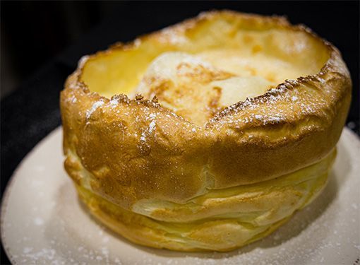 Fluffy, golden Dutch baby pancake with powdered sugar and a scoop of butter or ice cream on a white plate.